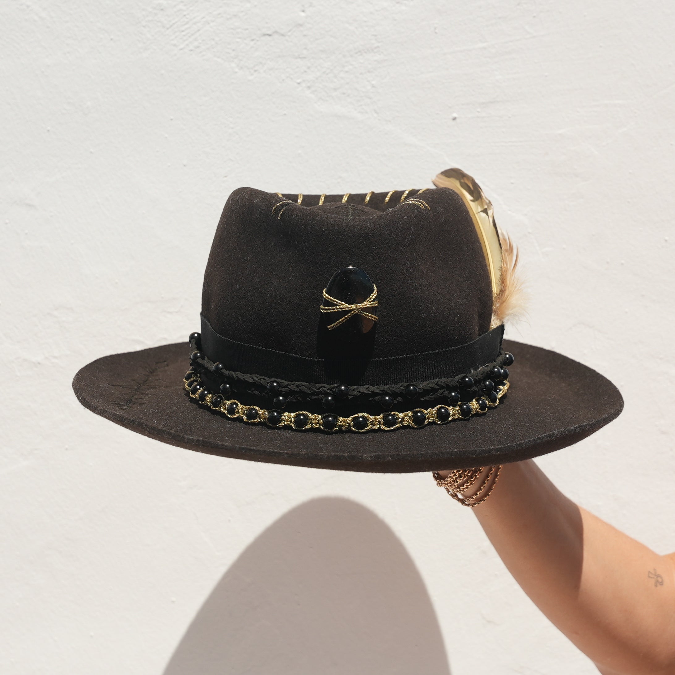 Close-up of Obsidian crystal and engraved arrow band on handcrafted black hat — Satori Collection